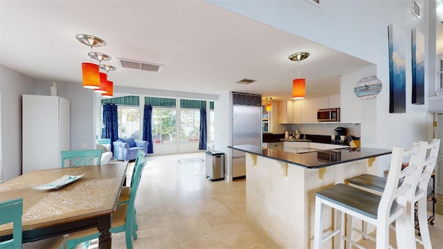 kitchen with a peninsula, a kitchen breakfast bar, white cabinets, appliances with stainless steel finishes, and dark countertops