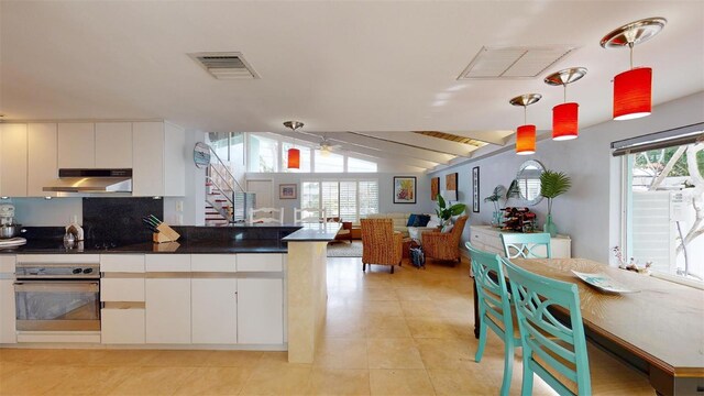 kitchen with hanging light fixtures, under cabinet range hood, stainless steel oven, and white cabinets