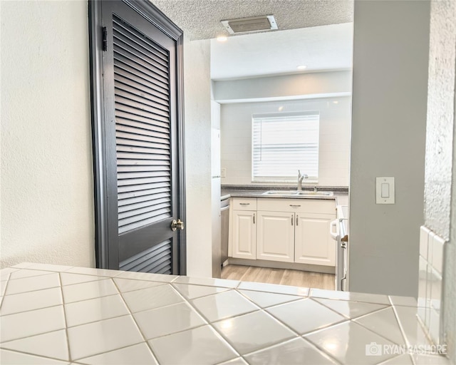 kitchen featuring dishwasher, tile countertops, sink, a textured ceiling, and light hardwood / wood-style floors