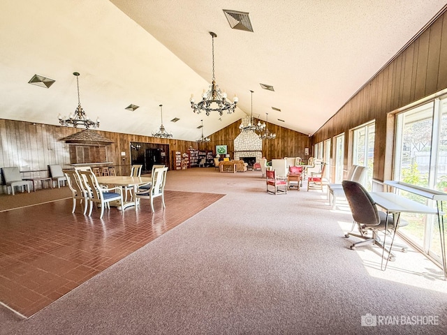 dining area featuring a large fireplace, wood walls, carpet flooring, and vaulted ceiling