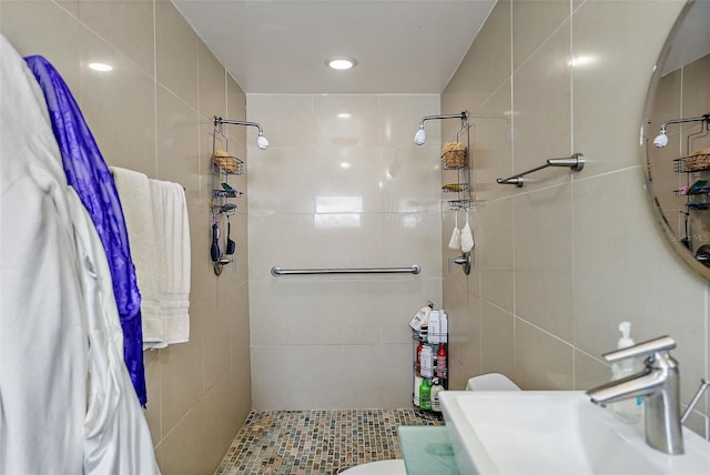 bathroom with tile walls, a sink, a tile shower, and toilet
