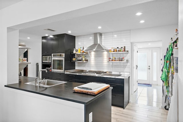 kitchen featuring wall chimney exhaust hood, dark cabinets, a sink, and open shelves