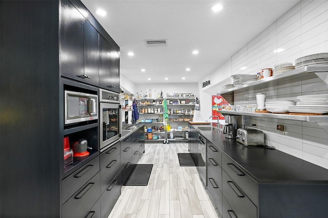 kitchen featuring tasteful backsplash, open shelves, stainless steel microwave, a sink, and dark countertops