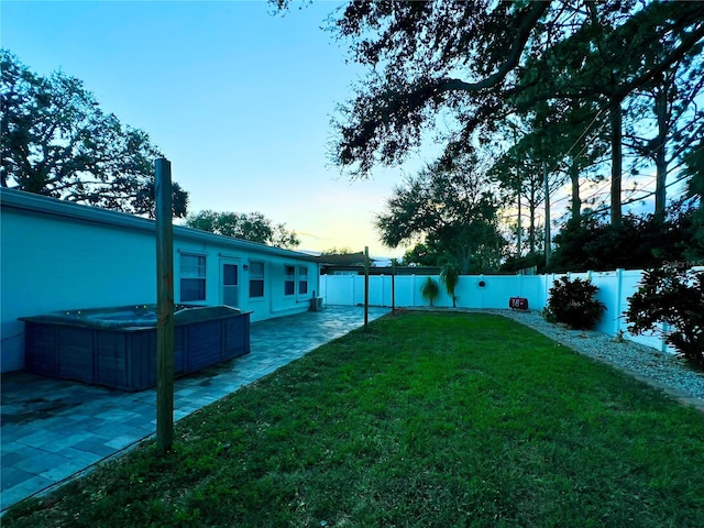 yard at dusk featuring a patio area, a hot tub, and a fenced backyard