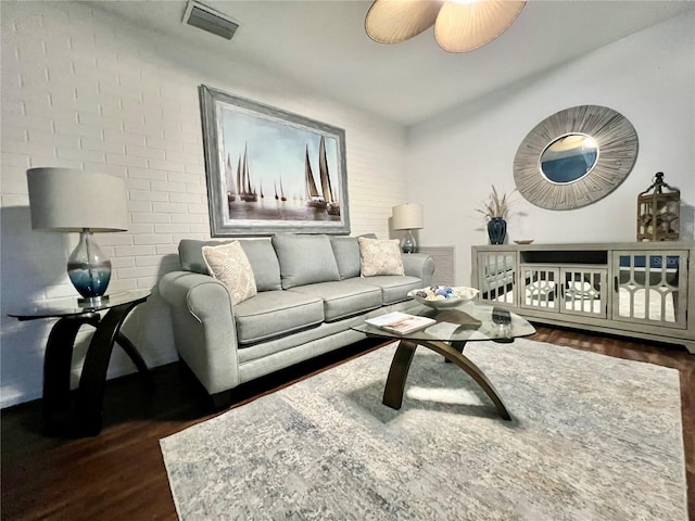 living room featuring ceiling fan, dark wood-type flooring, and brick wall