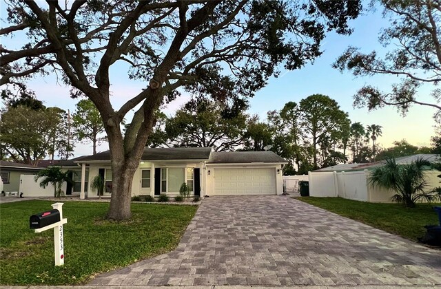 single story home featuring a garage, decorative driveway, fence, and a lawn