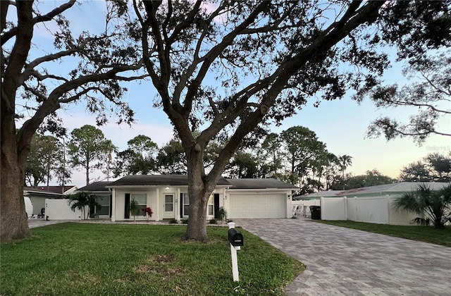 ranch-style house with an attached garage, fence, decorative driveway, and a yard