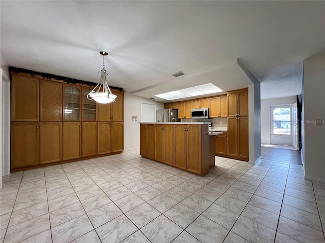 kitchen featuring glass insert cabinets, appliances with stainless steel finishes, brown cabinets, decorative light fixtures, and a center island