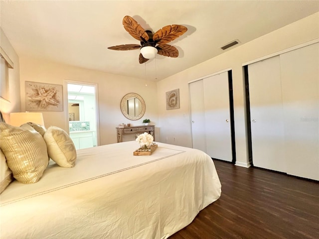 bedroom featuring dark wood-style flooring, two closets, visible vents, ceiling fan, and ensuite bath