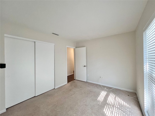 unfurnished bedroom featuring a closet, visible vents, light carpet, and baseboards