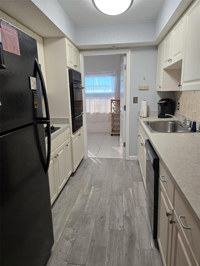 kitchen featuring white cabinetry, light hardwood / wood-style floors, black appliances, and sink