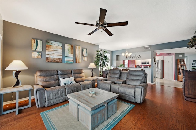 living room with ceiling fan with notable chandelier and dark hardwood / wood-style flooring