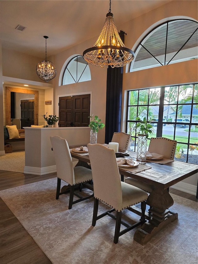 dining area with wood-type flooring, a towering ceiling, and a chandelier