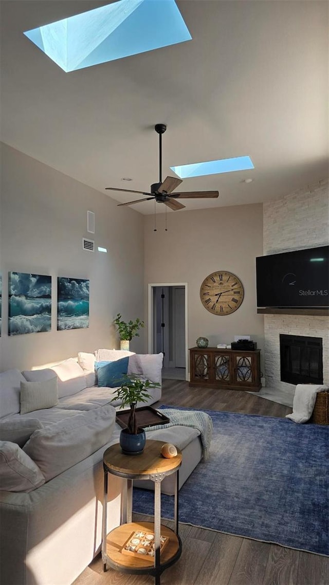 living room with a stone fireplace, high vaulted ceiling, a skylight, hardwood / wood-style flooring, and ceiling fan