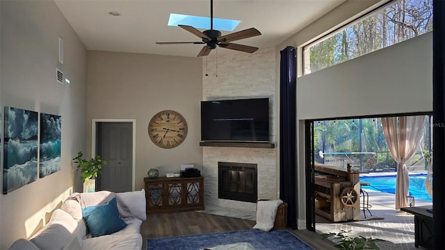 living room with a skylight, ceiling fan, a fireplace, hardwood / wood-style floors, and a high ceiling