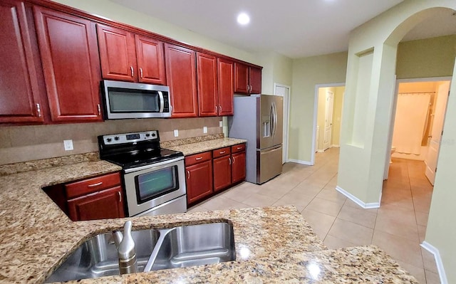 kitchen featuring stainless steel appliances, light stone countertops, light tile patterned floors, and sink