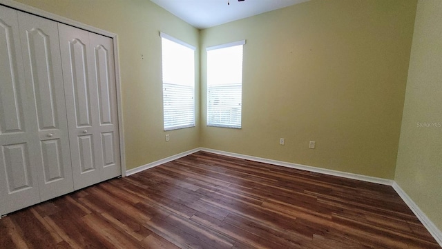 unfurnished bedroom with dark hardwood / wood-style flooring, a closet, and multiple windows