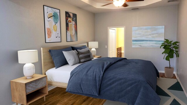 bedroom with dark wood-type flooring, ceiling fan, and a raised ceiling