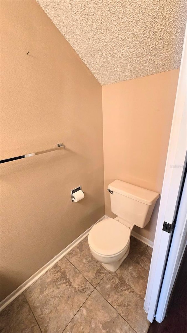 bathroom with tile patterned floors, vaulted ceiling, a textured ceiling, and toilet