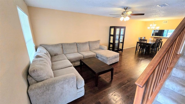 living room with ceiling fan with notable chandelier, a textured ceiling, dark wood-type flooring, and a healthy amount of sunlight