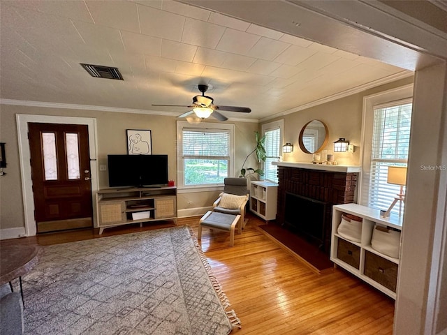 living room featuring a fireplace, ceiling fan, ornamental molding, and light hardwood / wood-style flooring