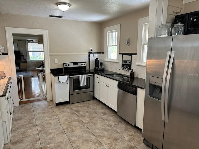 kitchen with stainless steel appliances, light tile patterned flooring, sink, white cabinets, and decorative backsplash