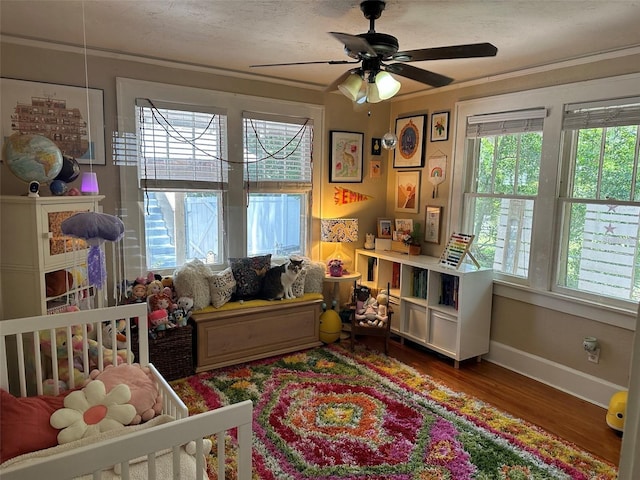 bedroom with a nursery area, multiple windows, ceiling fan, and dark hardwood / wood-style flooring