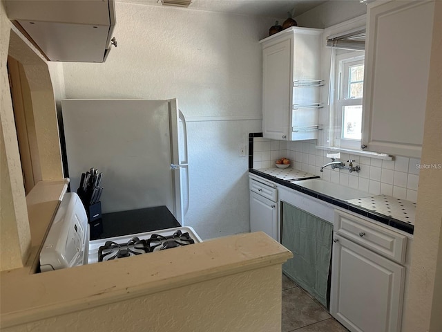 kitchen featuring sink, light tile patterned floors, backsplash, white cabinets, and white fridge