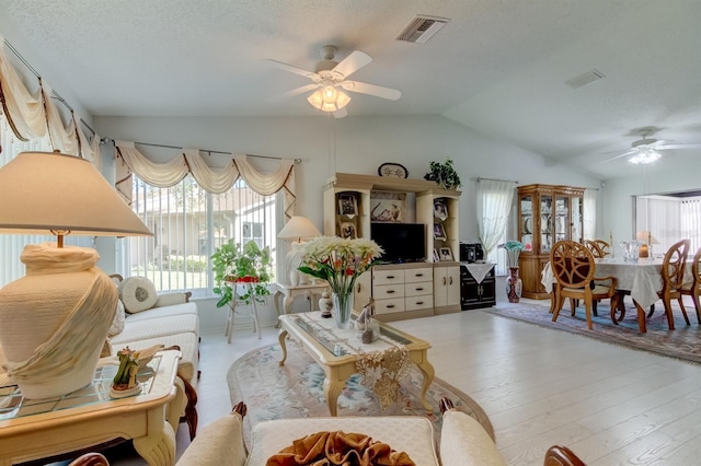 living room featuring light hardwood / wood-style floors, a textured ceiling, lofted ceiling, and ceiling fan