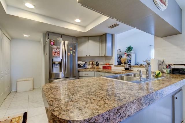 kitchen featuring decorative backsplash, stainless steel refrigerator with ice dispenser, a tray ceiling, kitchen peninsula, and sink