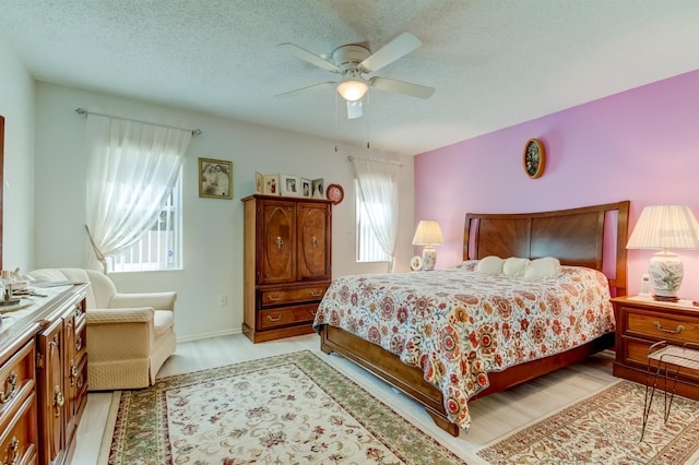 bedroom featuring ceiling fan, a textured ceiling, multiple windows, and light wood-type flooring