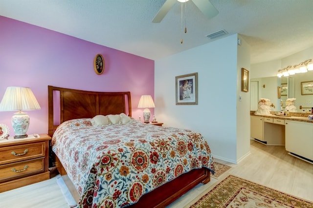 bedroom with ceiling fan, a textured ceiling, ensuite bathroom, and light wood-type flooring