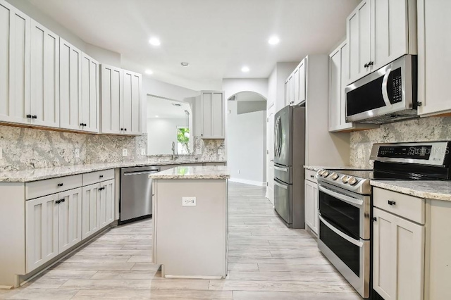 kitchen featuring appliances with stainless steel finishes, light hardwood / wood-style floors, a kitchen island, and light stone countertops