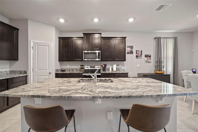 kitchen featuring appliances with stainless steel finishes, sink, dark brown cabinetry, and an island with sink