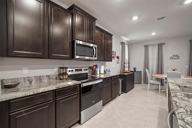 kitchen featuring stainless steel appliances, dark brown cabinetry, and light stone countertops