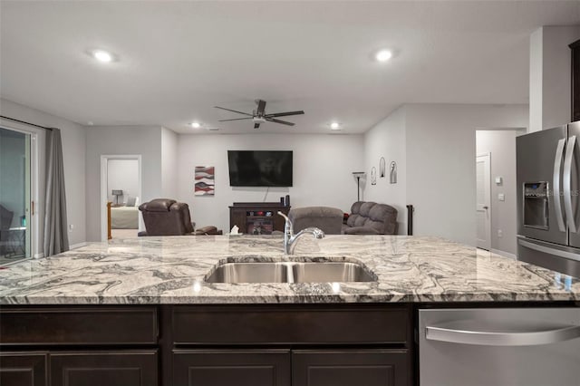 kitchen featuring appliances with stainless steel finishes, sink, a kitchen island with sink, ceiling fan, and light stone counters