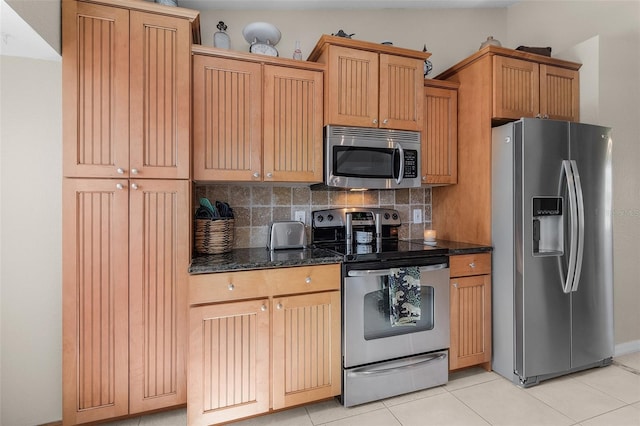 kitchen featuring decorative backsplash, dark stone countertops, vaulted ceiling, light tile patterned floors, and appliances with stainless steel finishes