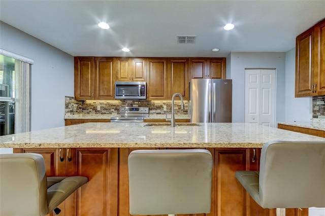 kitchen with a kitchen bar, appliances with stainless steel finishes, light stone counters, a kitchen island with sink, and sink