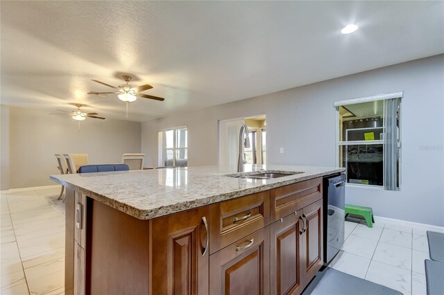 kitchen featuring a textured ceiling, ceiling fan, a kitchen island with sink, sink, and black dishwasher