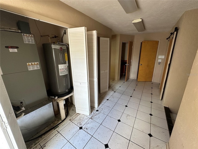 interior space featuring heating unit, a textured ceiling, and electric water heater