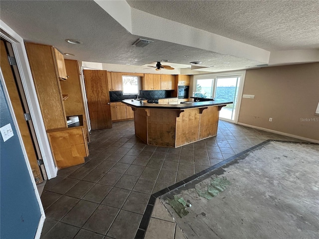 kitchen with dark countertops, oven, baseboards, a kitchen breakfast bar, and brown cabinetry