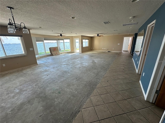 interior space featuring ceiling fan with notable chandelier, plenty of natural light, a water view, and a textured ceiling