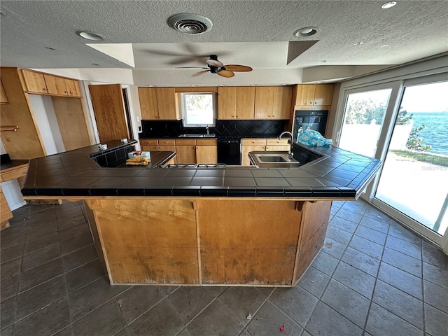 kitchen with black appliances, tile counters, visible vents, and a sink