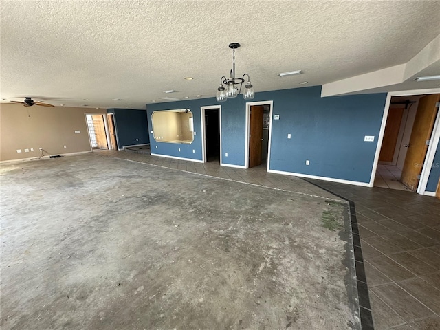 unfurnished living room with ceiling fan with notable chandelier, a textured ceiling, and baseboards