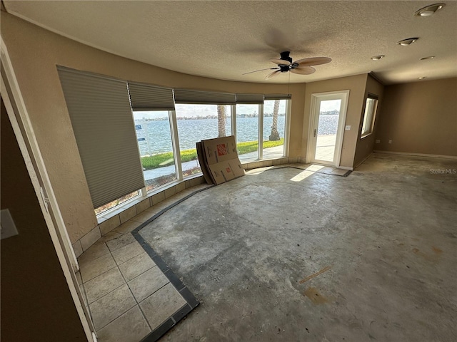 unfurnished living room with concrete floors, baseboards, ceiling fan, a water view, and a textured ceiling