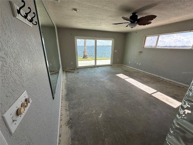 spare room featuring a textured ceiling, a wealth of natural light, a water view, and ceiling fan