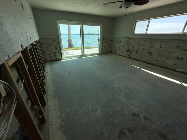 empty room featuring a water view, a textured ceiling, and ceiling fan