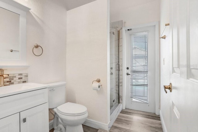 bathroom featuring wood-type flooring, a shower with shower door, toilet, vanity, and decorative backsplash