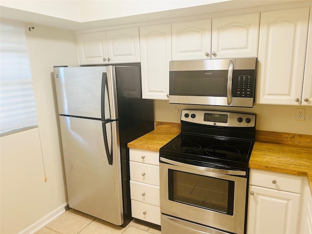 kitchen featuring white cabinets, appliances with stainless steel finishes, light tile patterned floors, and butcher block countertops