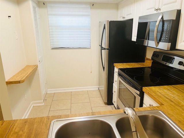 kitchen with stainless steel appliances, light tile patterned flooring, white cabinetry, sink, and wood counters